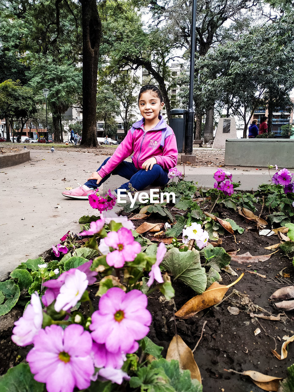 PORTRAIT OF SMILING WOMAN WITH PINK FLOWERS AGAINST TREES