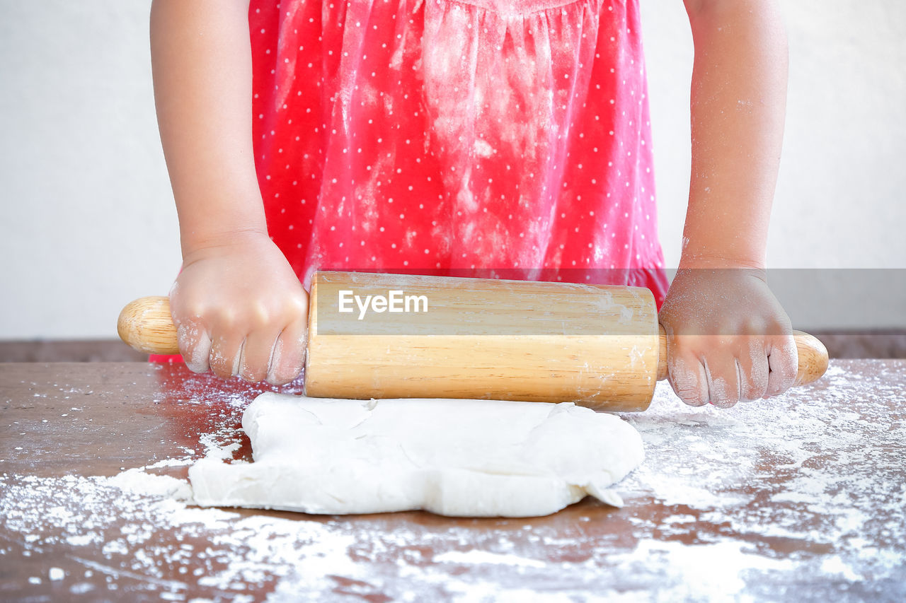 Midsection of girl preparing dough with rolling pin on table