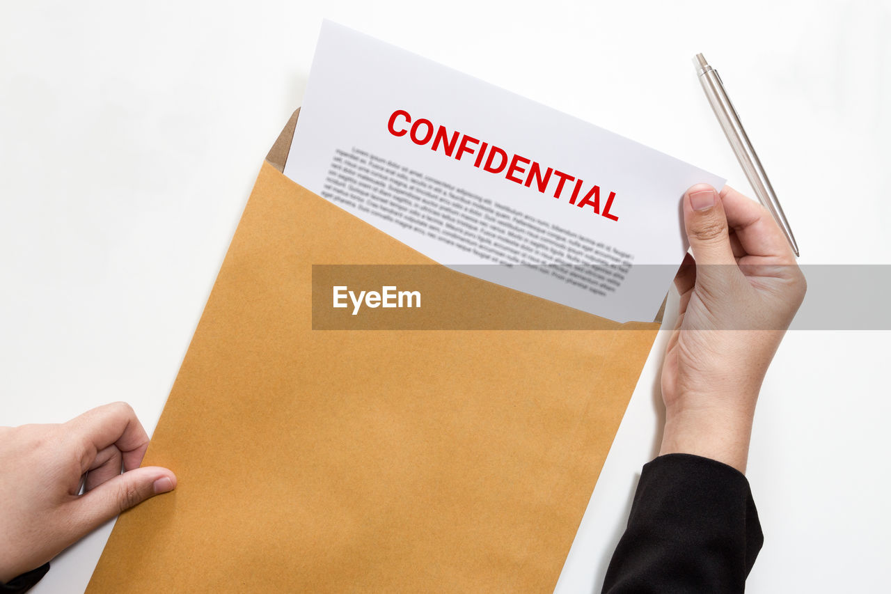 Cropped hands of businesswoman removing document from envelope over white background