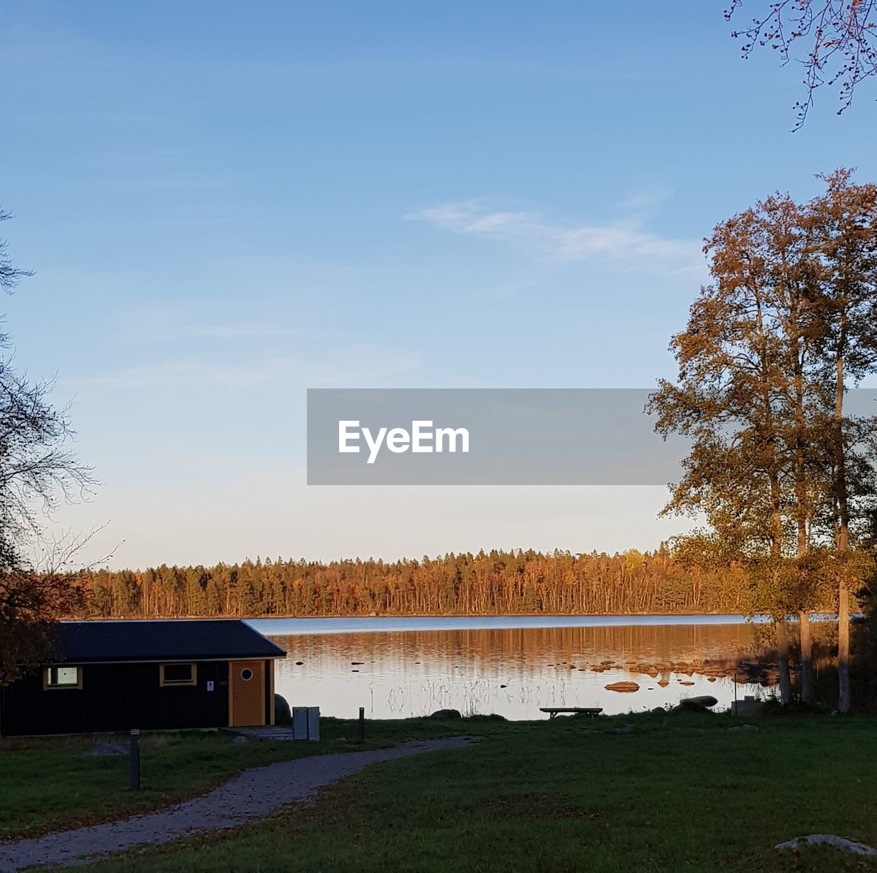 House on field by lake against sky