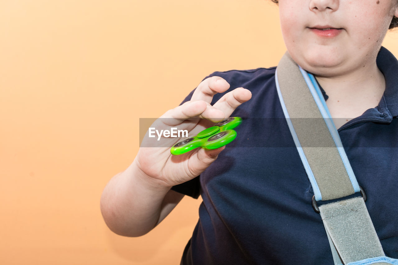 Midsection of boy holding fidget spinner against yellow background