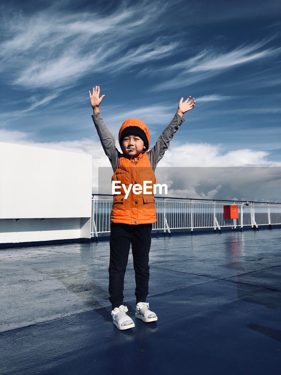 Full length of cute boy standing with arms raised on pier