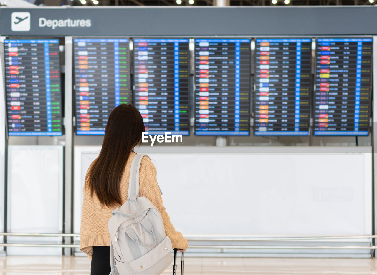 Woman looking at the flight information board, checking her flight at the airport traveling concept.