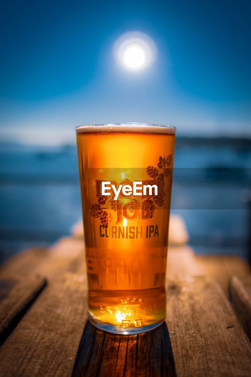 CLOSE-UP OF BEER GLASS ON TABLE BY SEA