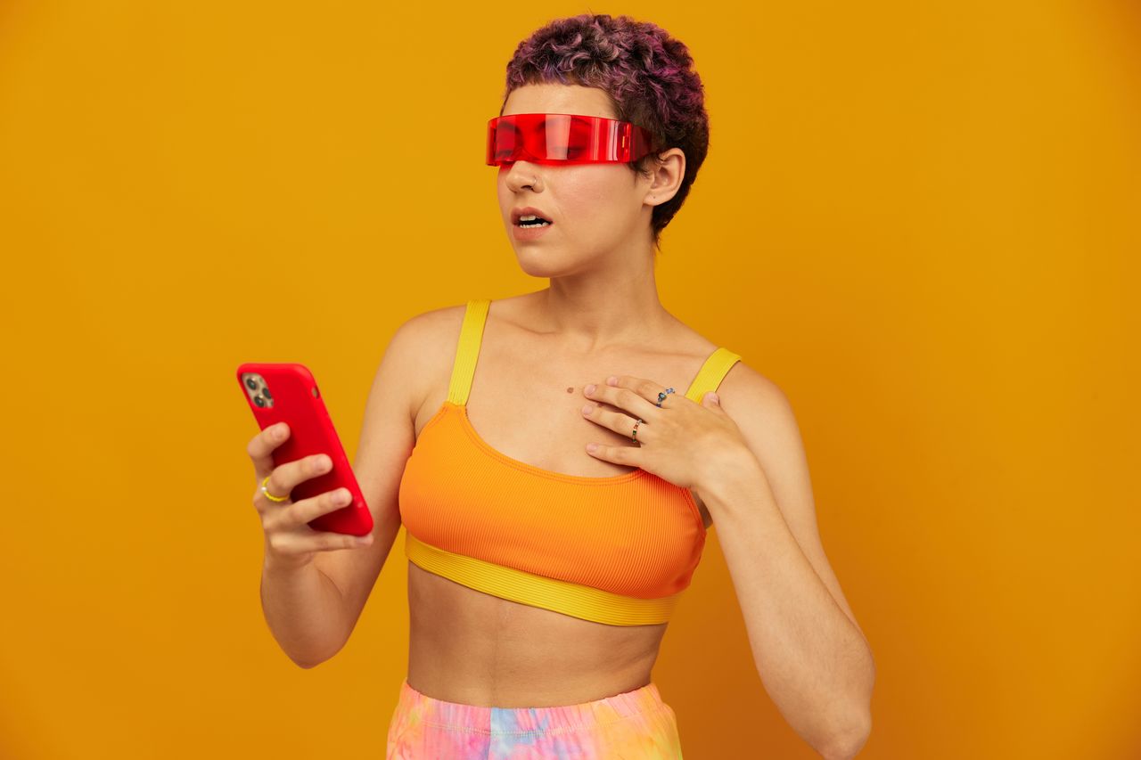 portrait of young woman with mobile phone while standing against yellow background