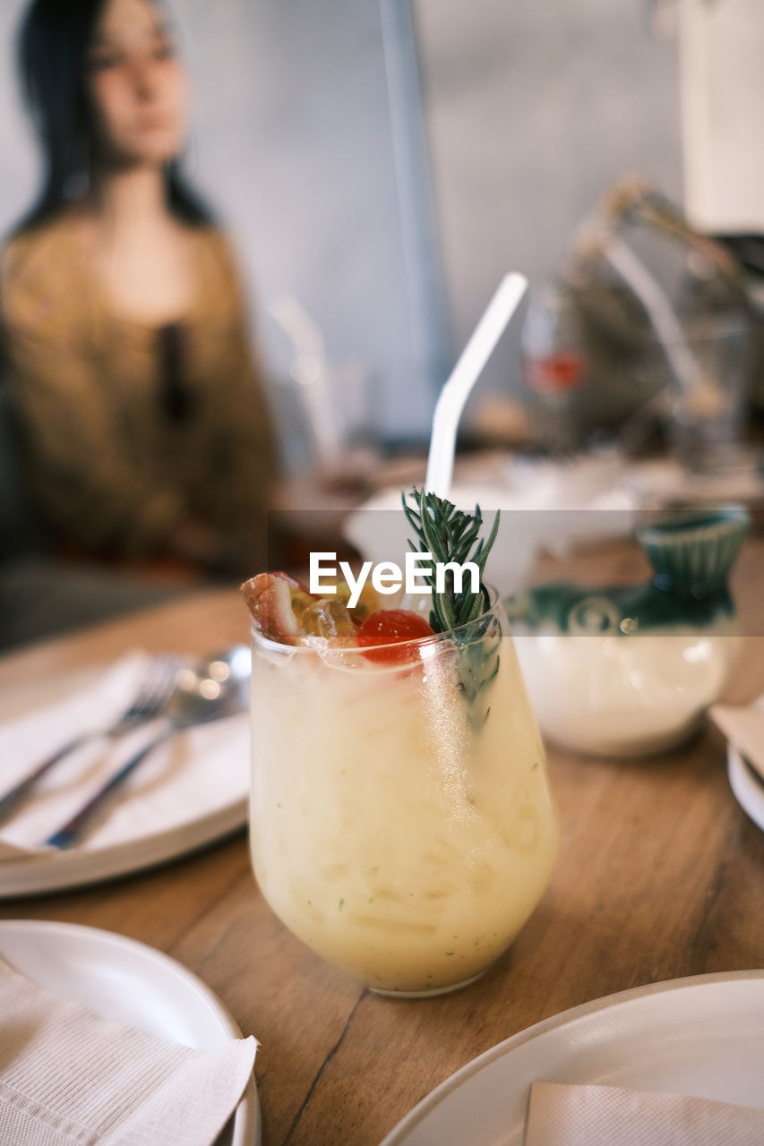 Close-up of drink in glass on table with woman in background