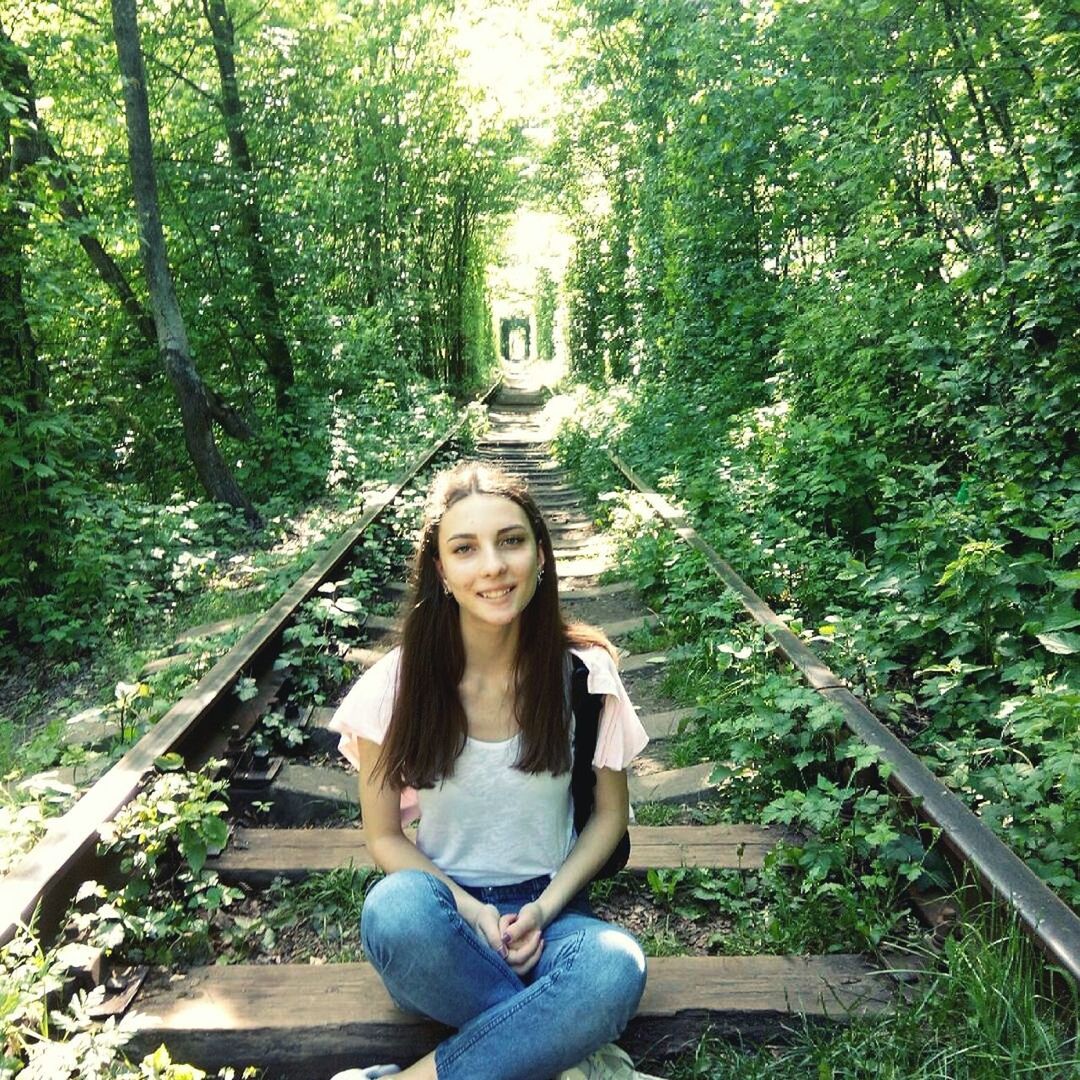 Portrait of young woman sitting amidst railroad track in forest