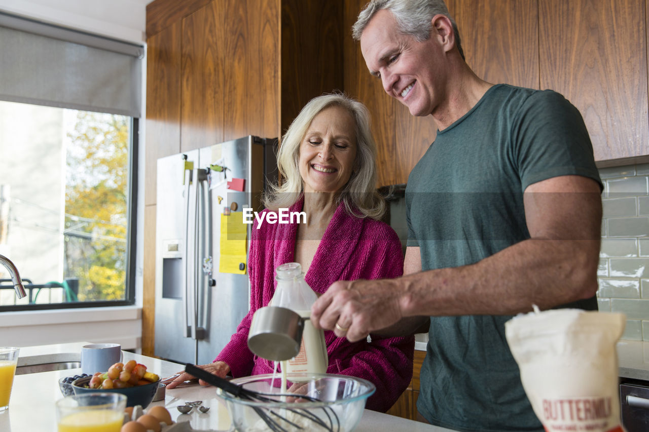 Man preparing food while standing by smiling woman in kitchen at home