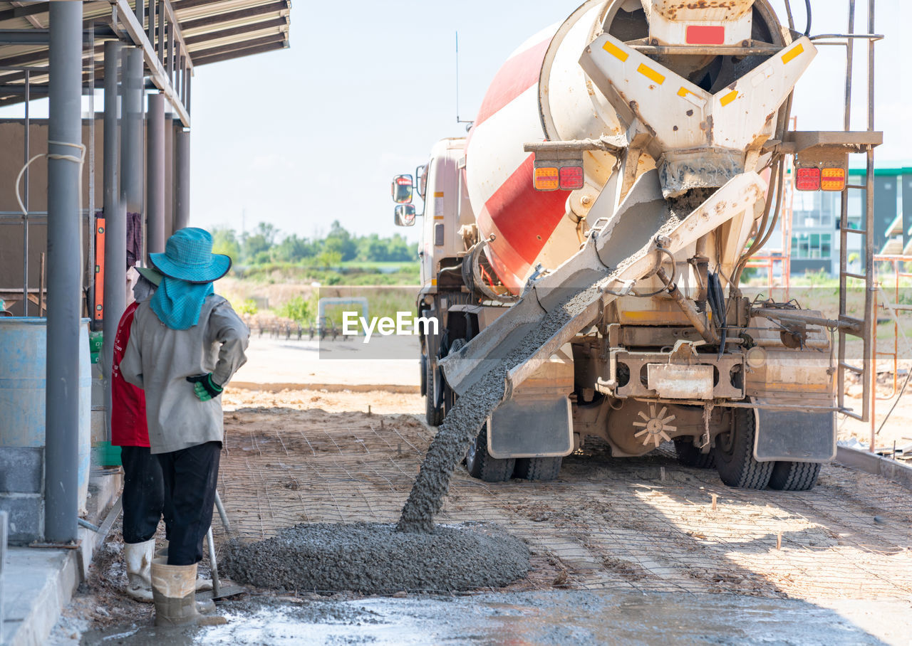 Concrete mixer truck pouring concrete on floor in construction site and worker waiting for screed.