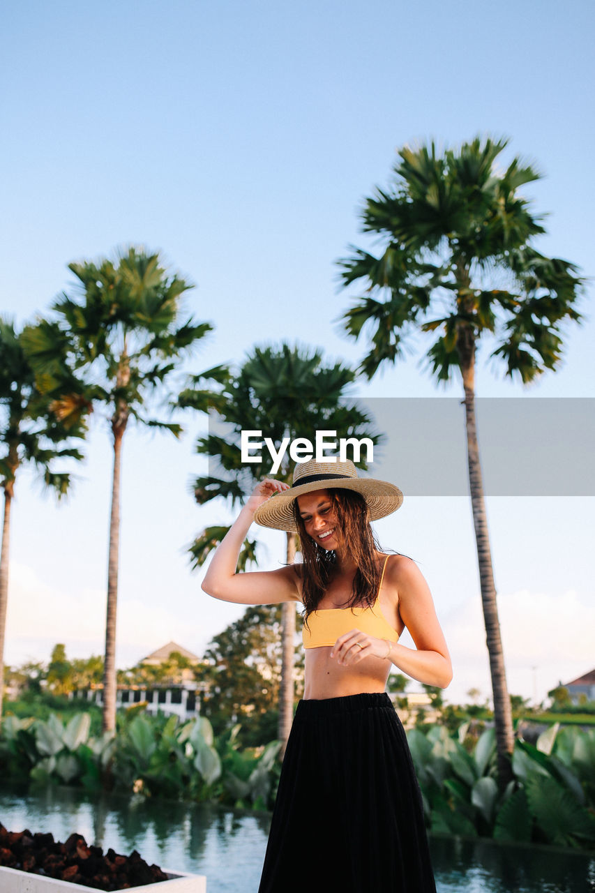 Smiling young woman standing against palm trees