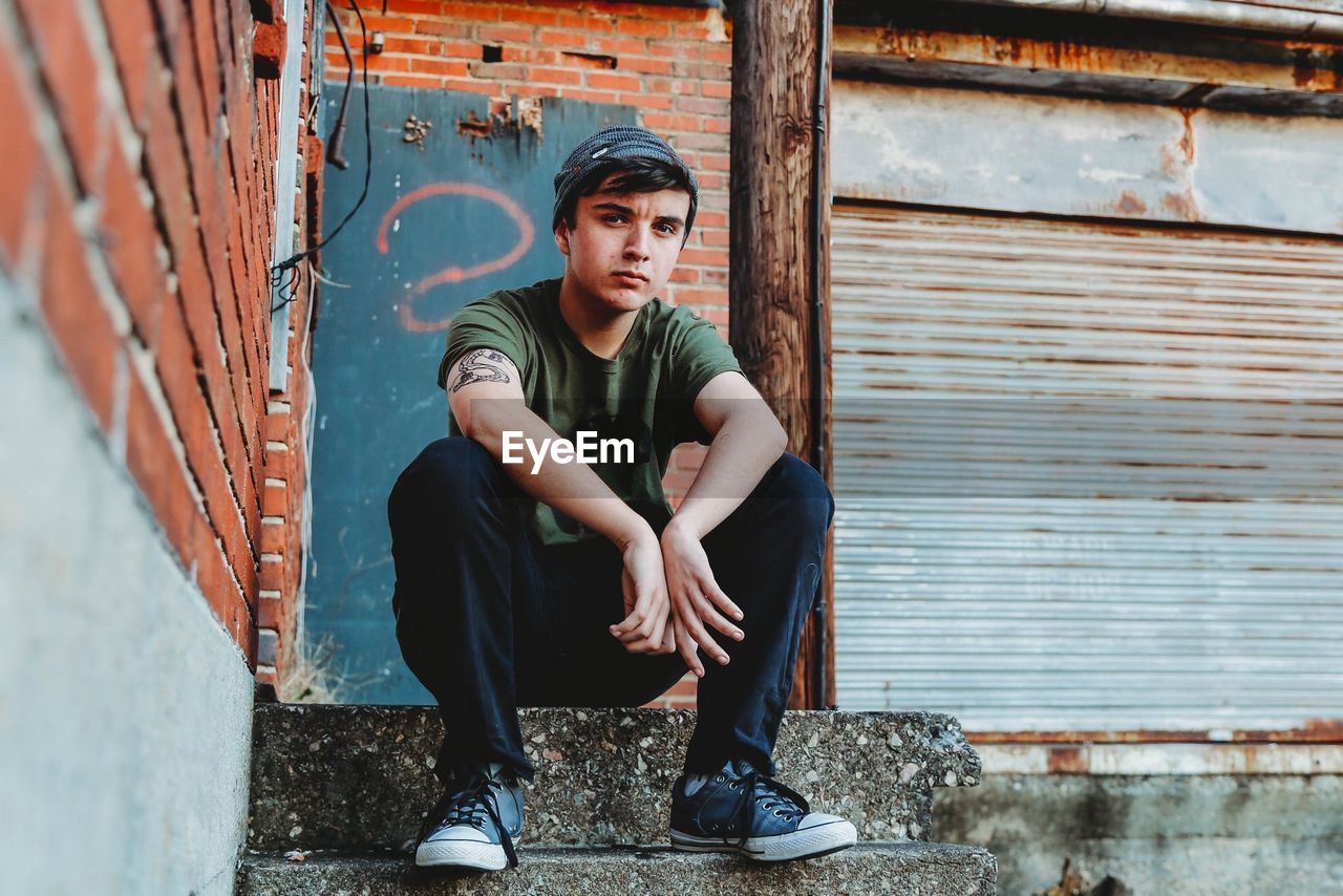 Portrait of teenage boy sitting on steps against wall