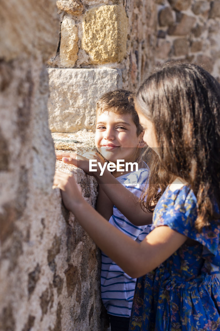 Siblings standing by stone wall