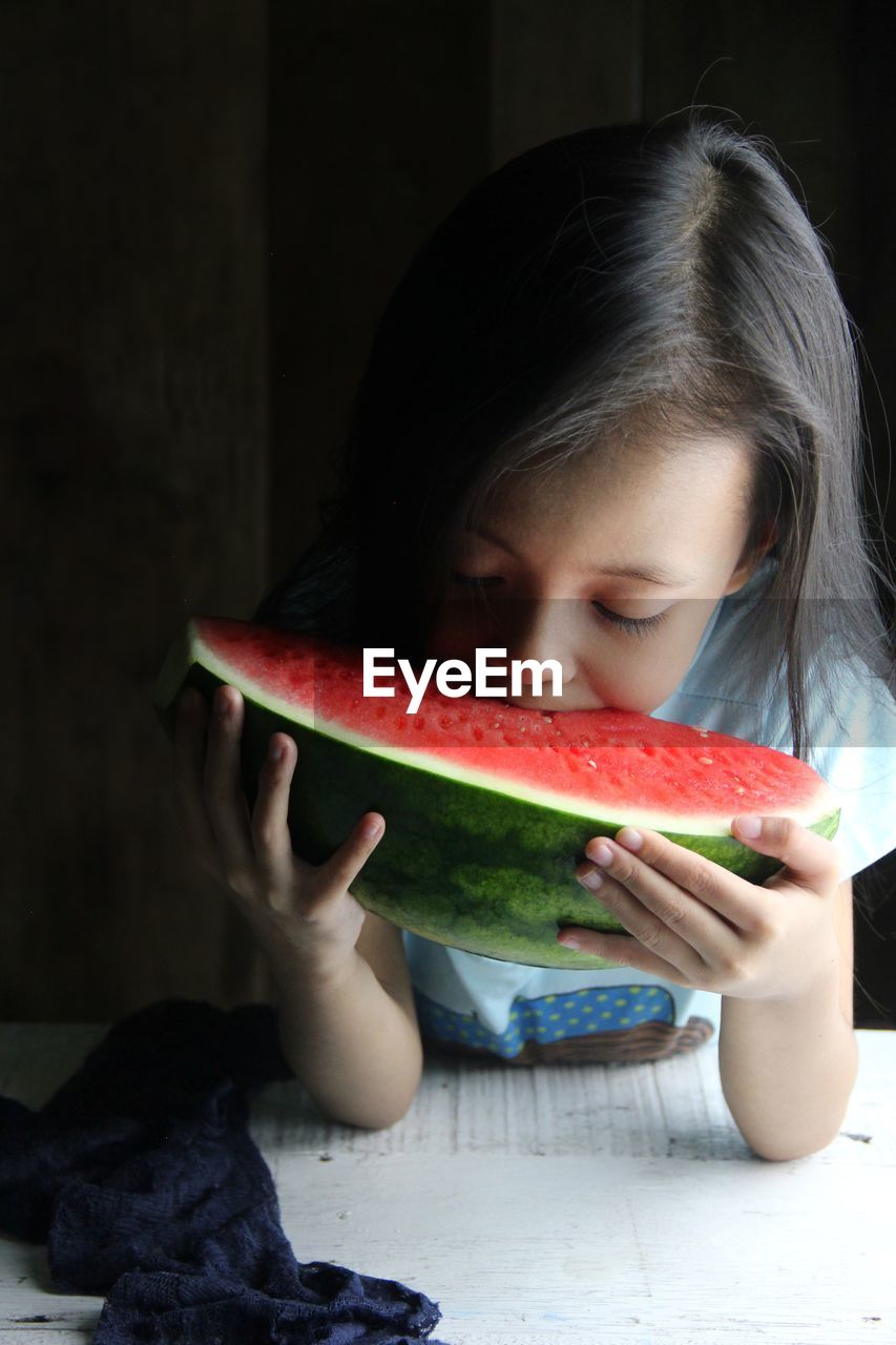 Close-up of little girl eating juicy watermelon against dark background