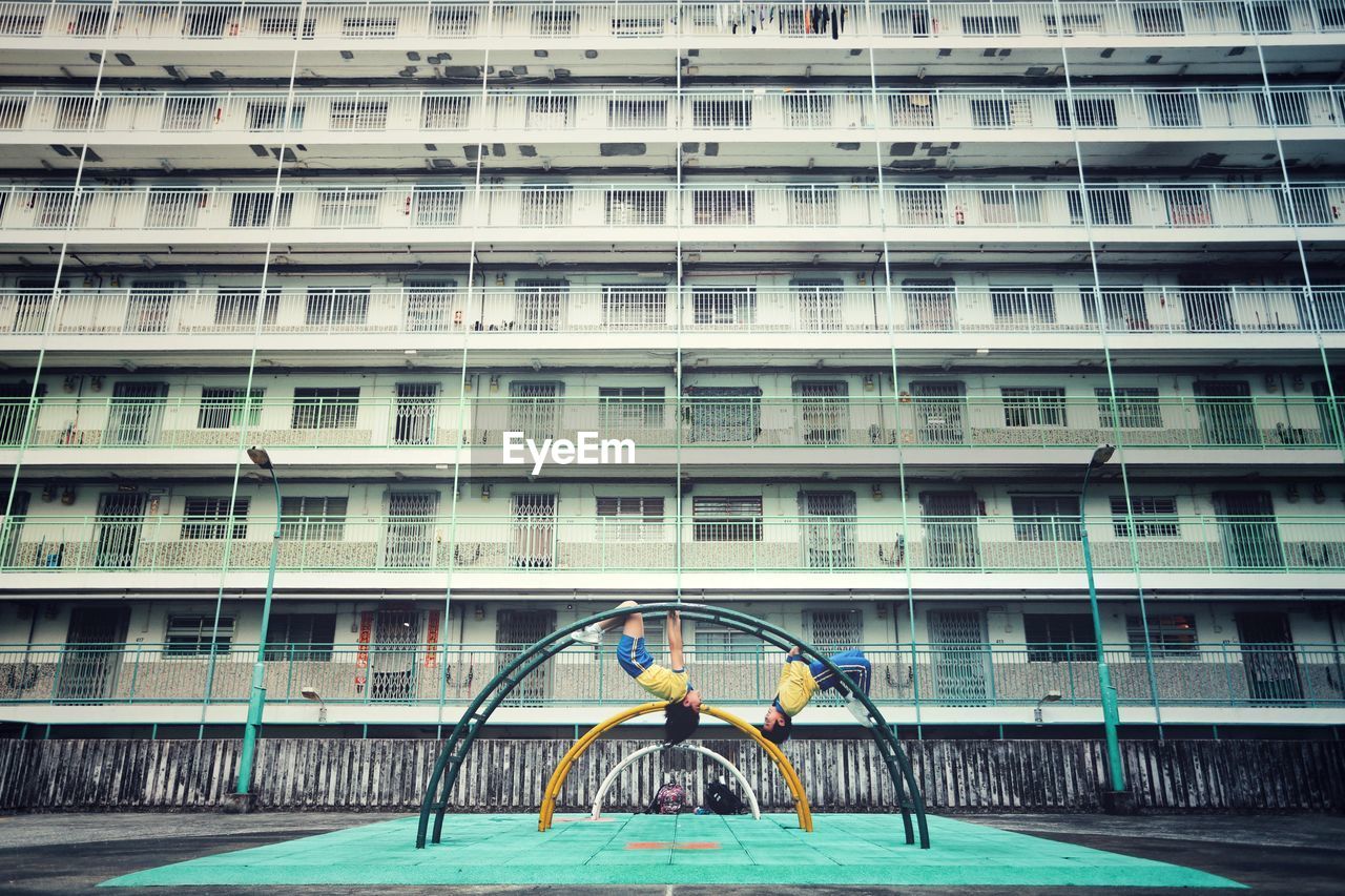 Siblings hanging on play equipment against building