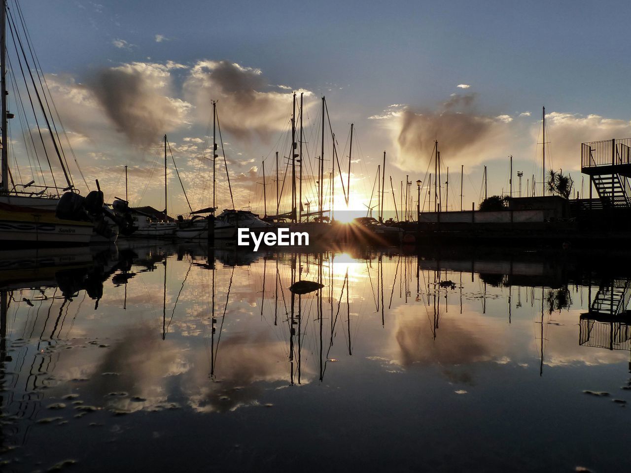 Sailboats moored at harbor against sky during sunset