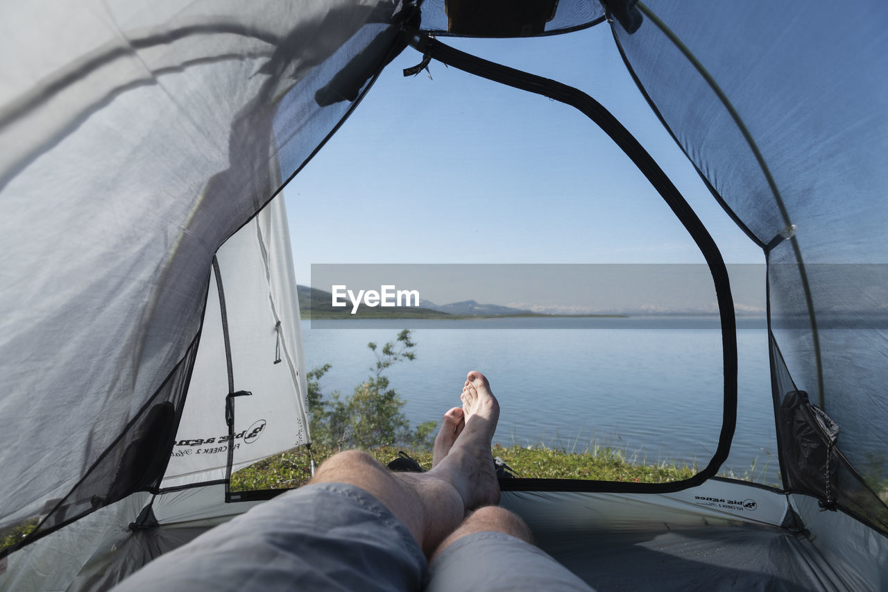 Legs of male backpacker in tent with view over lake virihaure from staloluokta, padjelantaleden trail, padjelanta national park, sweden