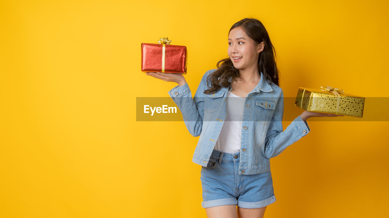 WOMAN STANDING AGAINST YELLOW BACKGROUND