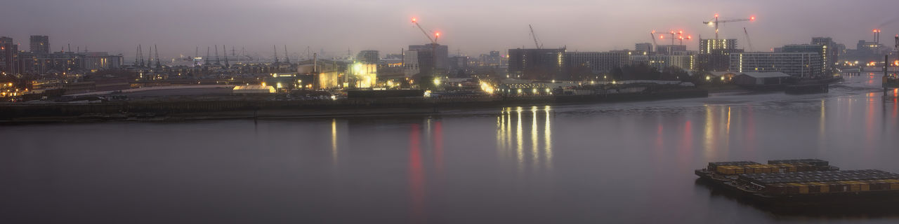 ILLUMINATED BUILDINGS BY RIVER AGAINST SKY