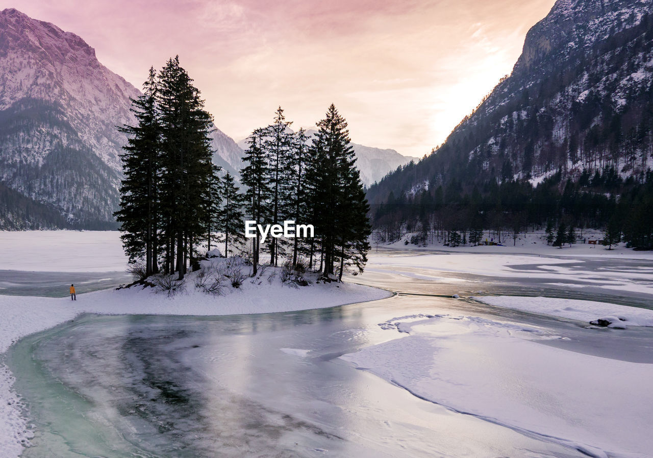 Person standing on frozen sea against trees and mountains