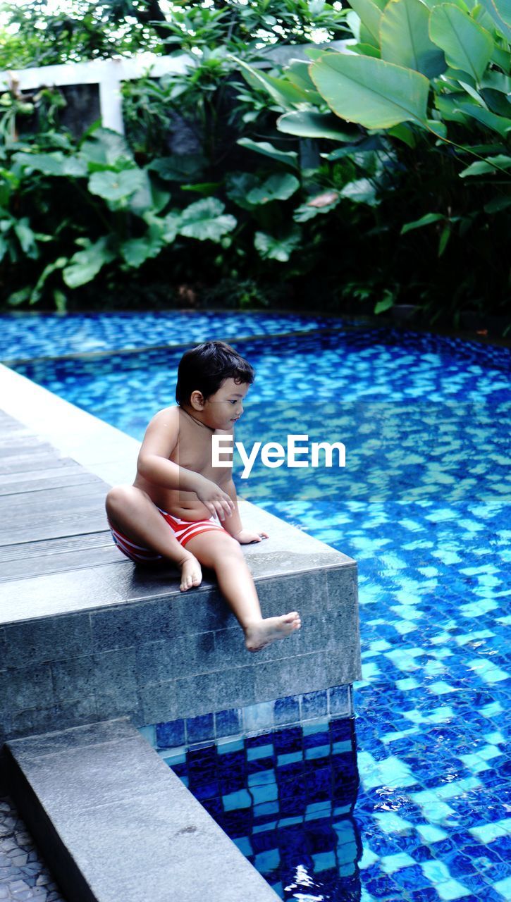 Side view of a boy sitting on poolside