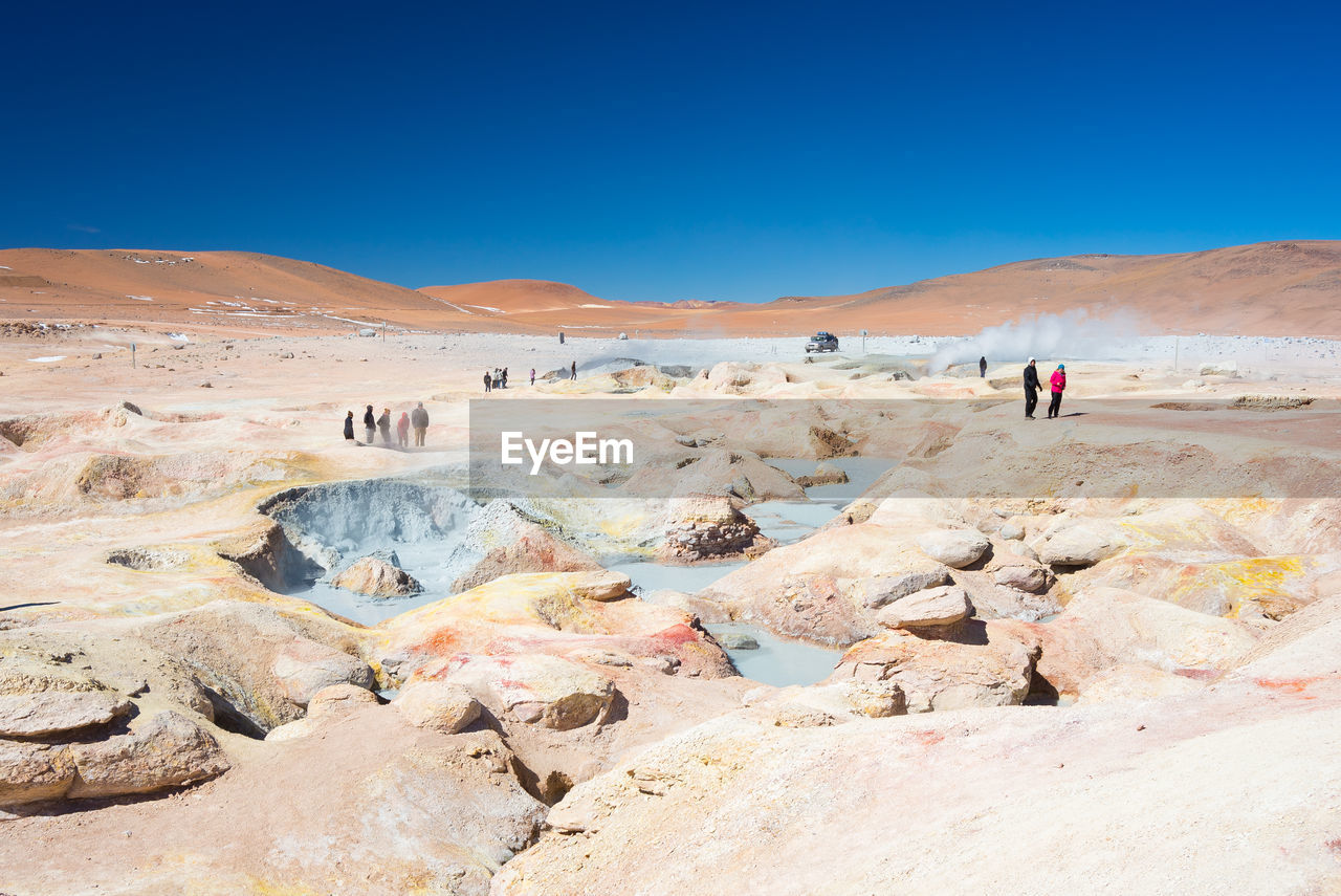 People by mud pots on landscape against clear sky