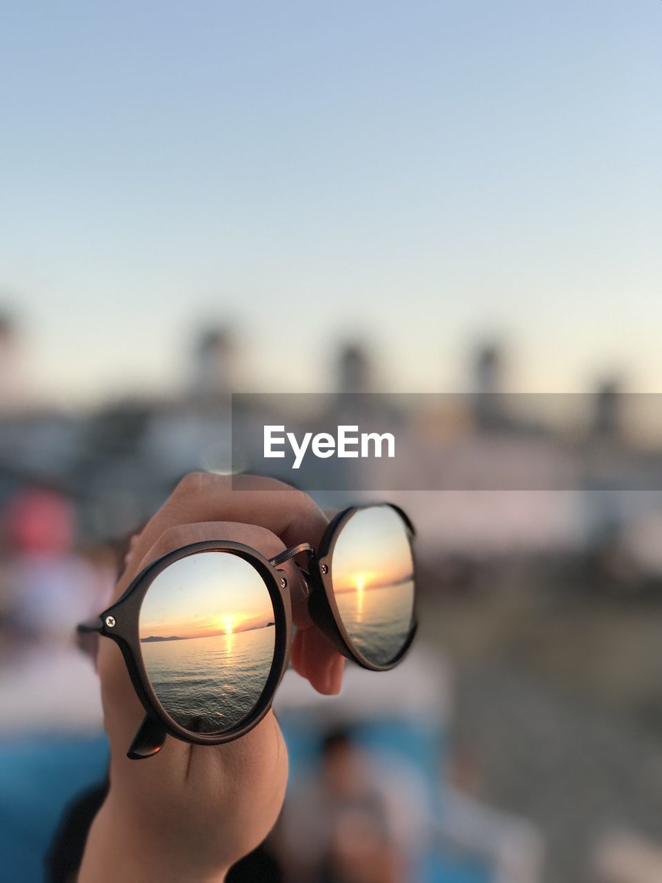 Close-up of hand holding eyeglasses against sky