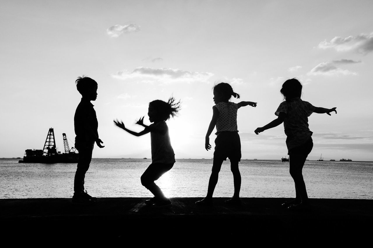 Silhouette children standing on beach against sky