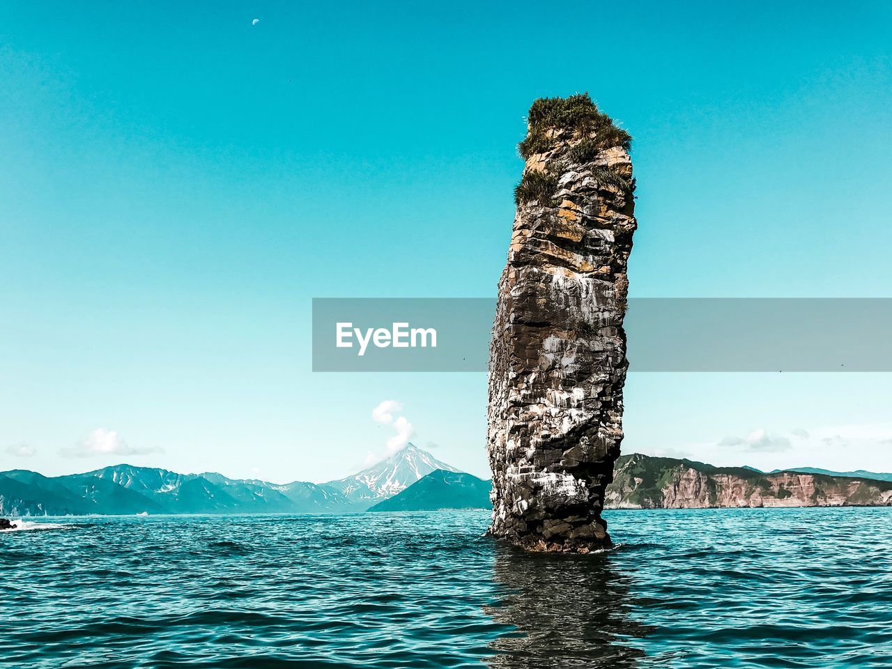 View of rock in sea against clear blue sky