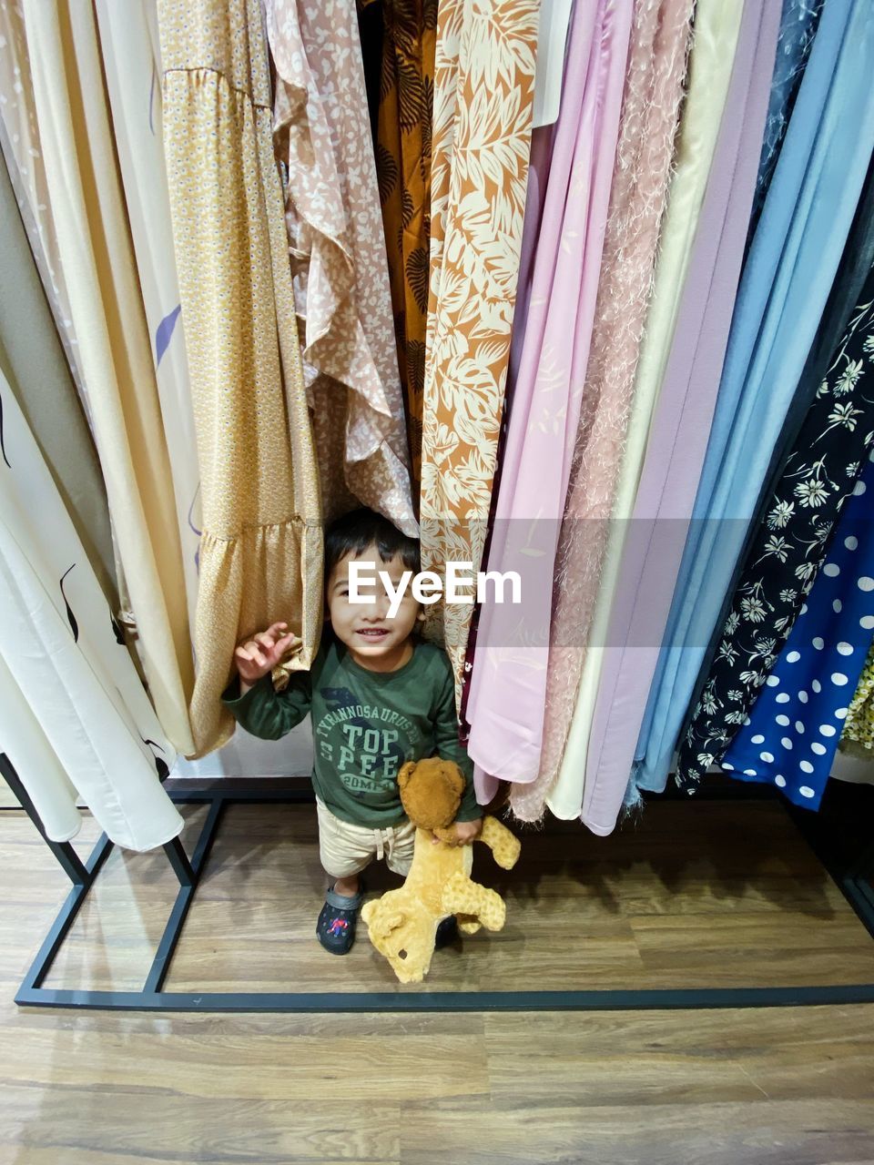 High angle view portrait of boy with stuffed toy by clothing at home