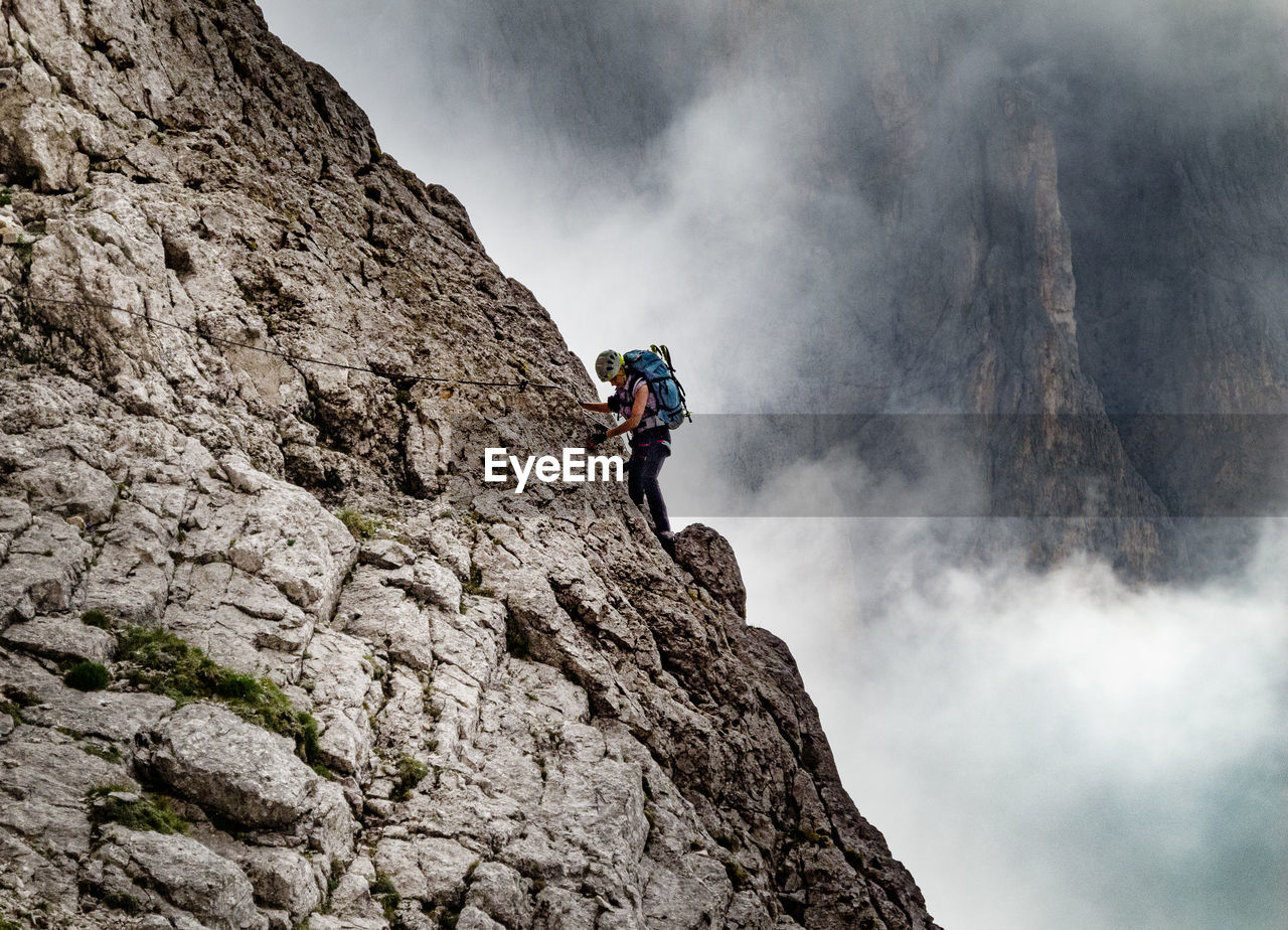 Low angle view of woman climbing on mountain against sky