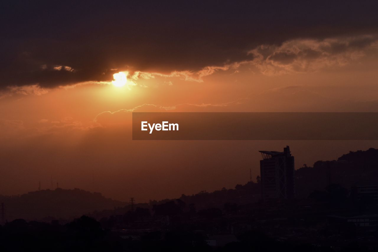 SILHOUETTE BUILDINGS IN CITY AGAINST SKY DURING SUNSET