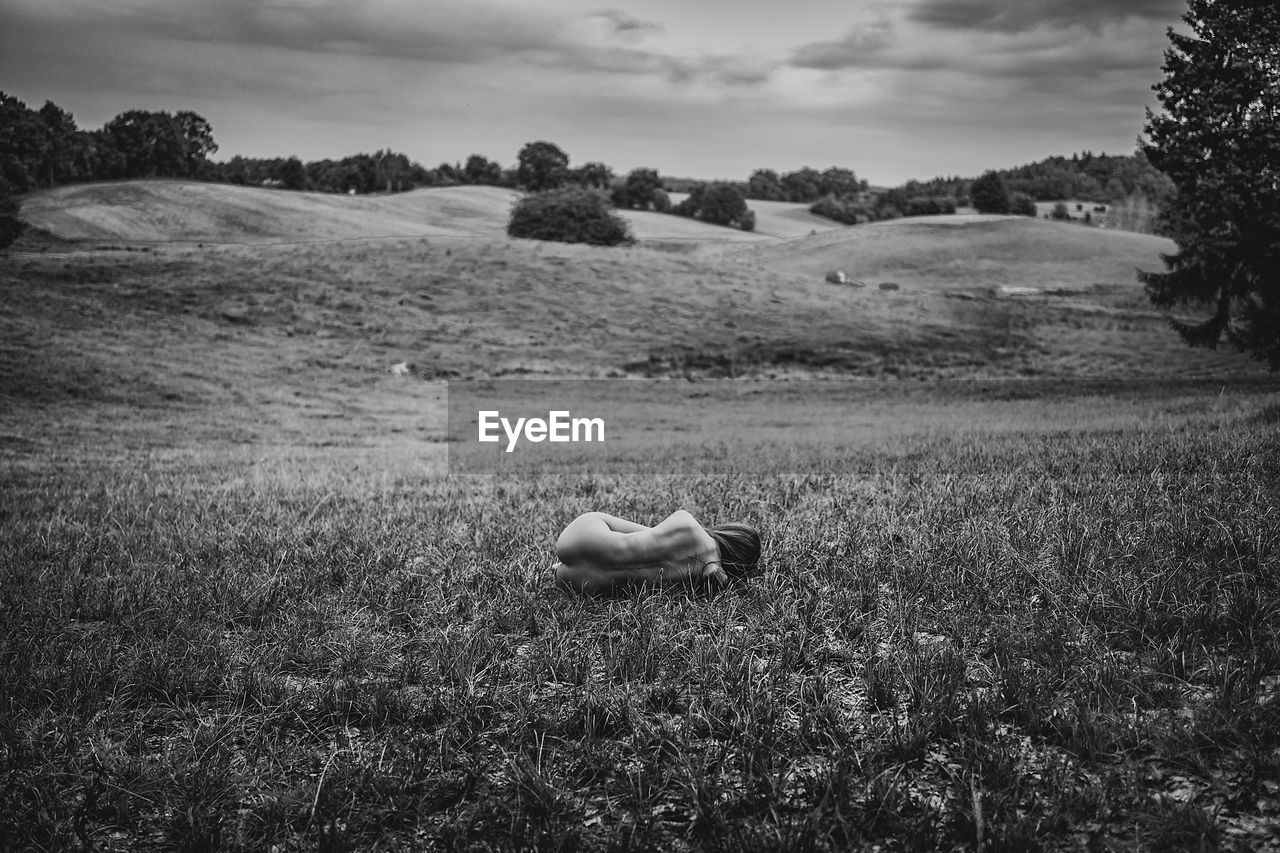 Rear view of depressed naked woman lying on grassy field