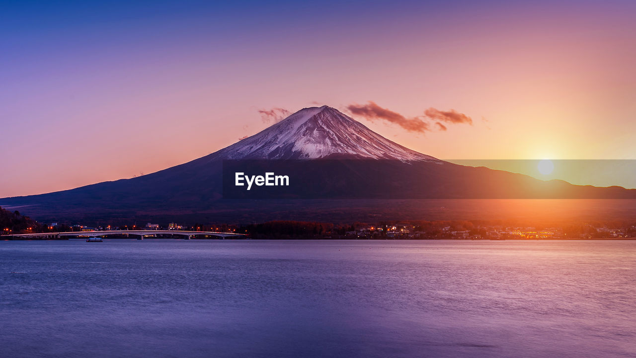 Scenic view of lake against snowcapped mountains during sunset