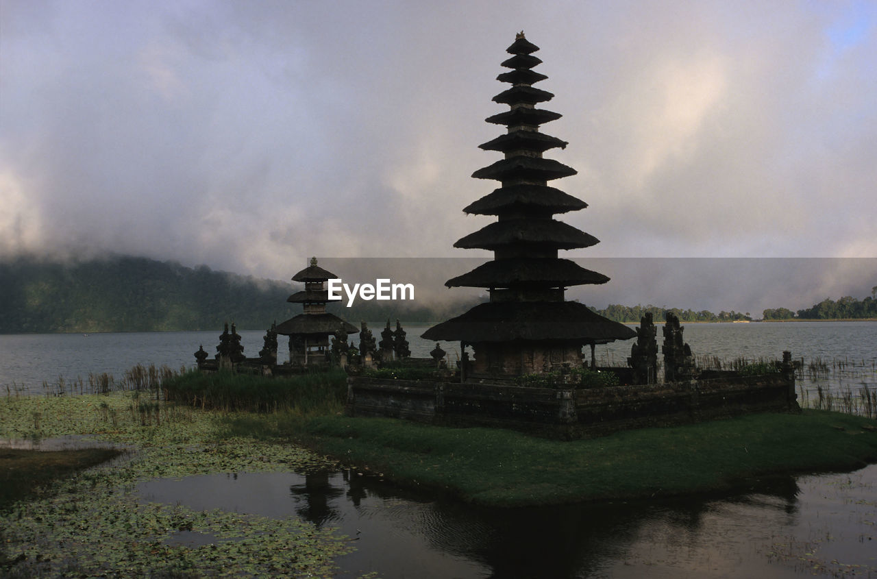 Pagoda by lake against cloudy sky