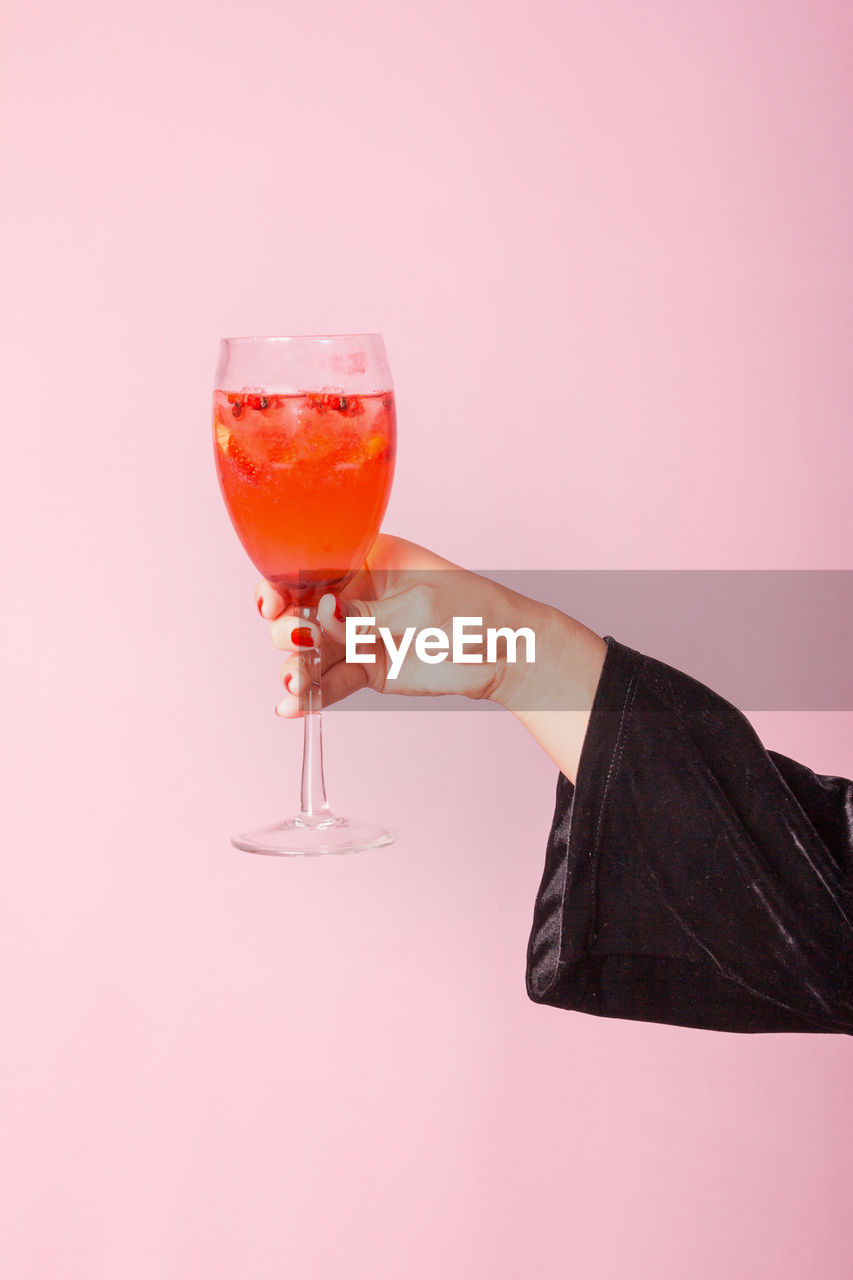 Female hand holding drink against light pink background.