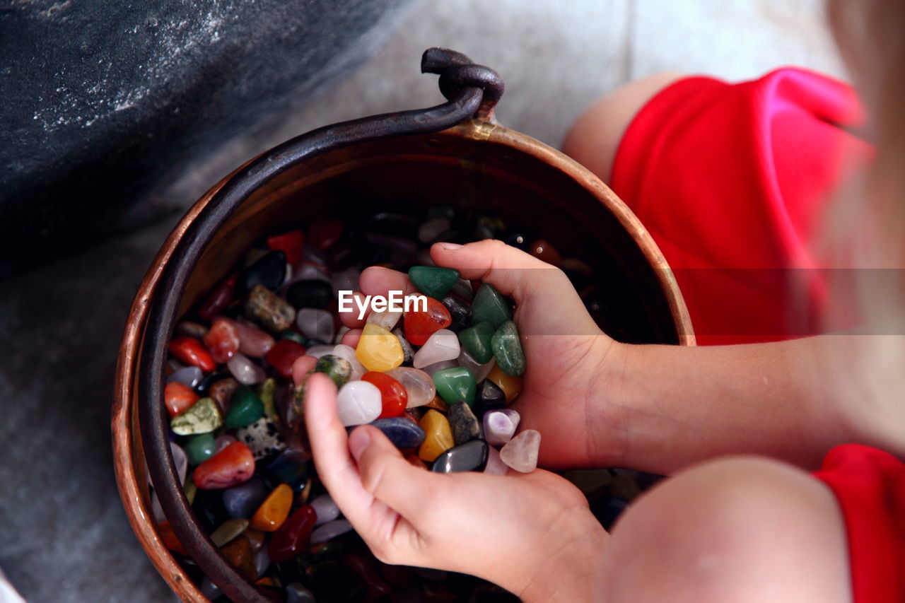 Midsection of boy holding colorful stones over bucket