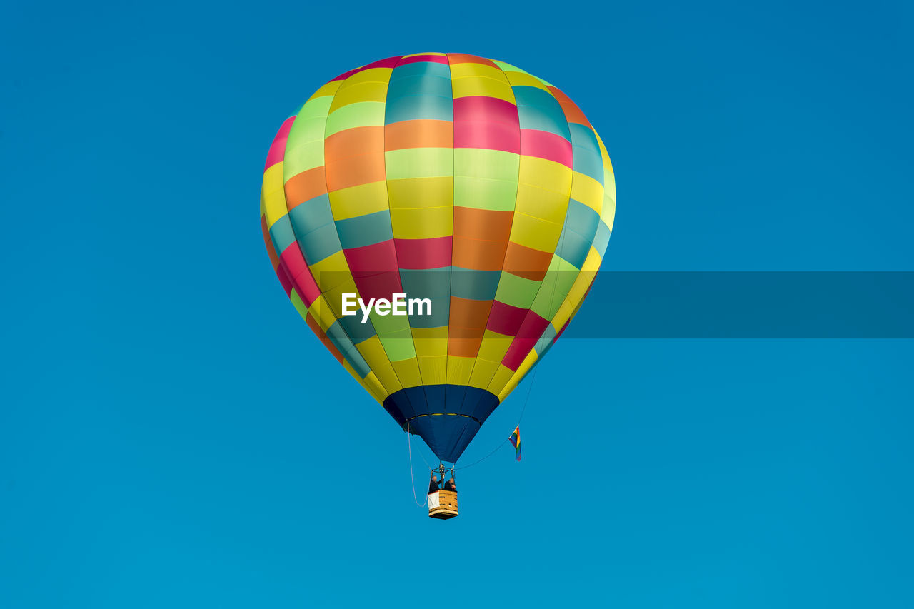 Low angle view of man and woman in hot air balloon against clear blue sky