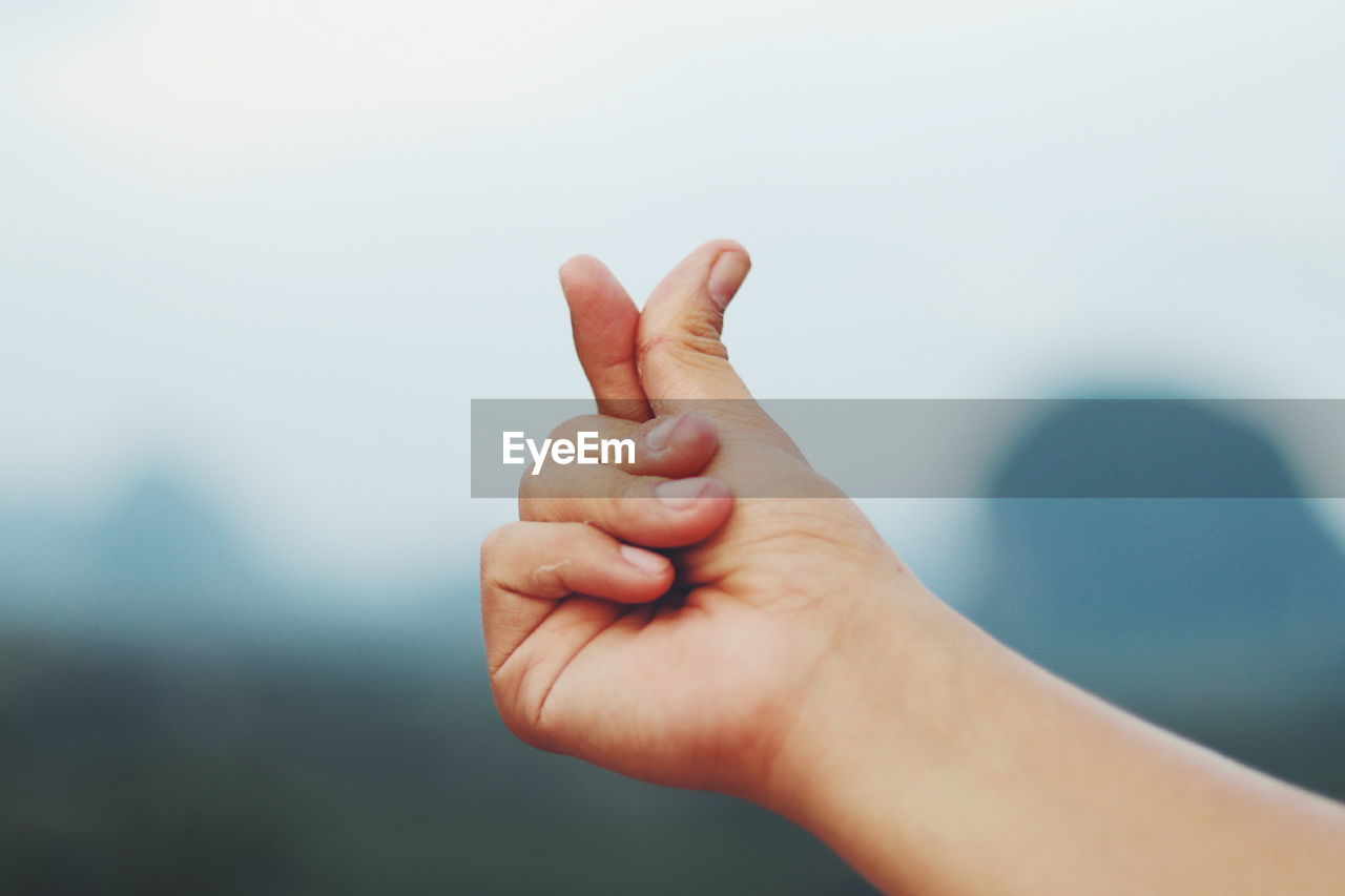 Close-up of cropped hand gesturing against clear sky