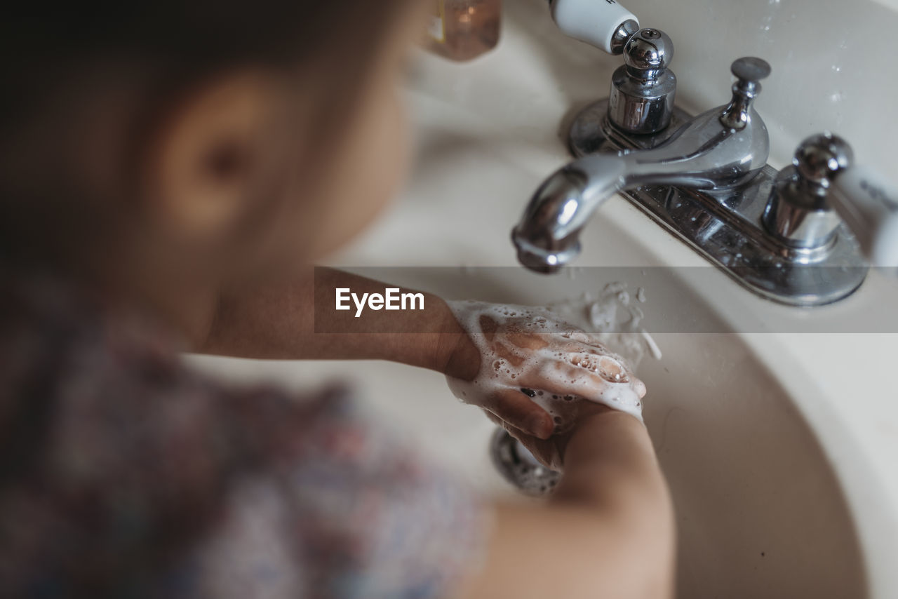 High angle of preschool aged girl washing hands in sink with soap