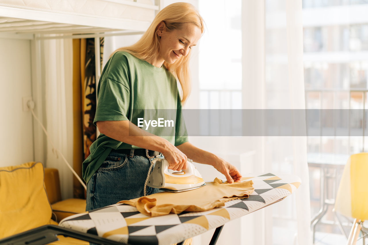 Middle-aged woman housewife ironing clothes at home.