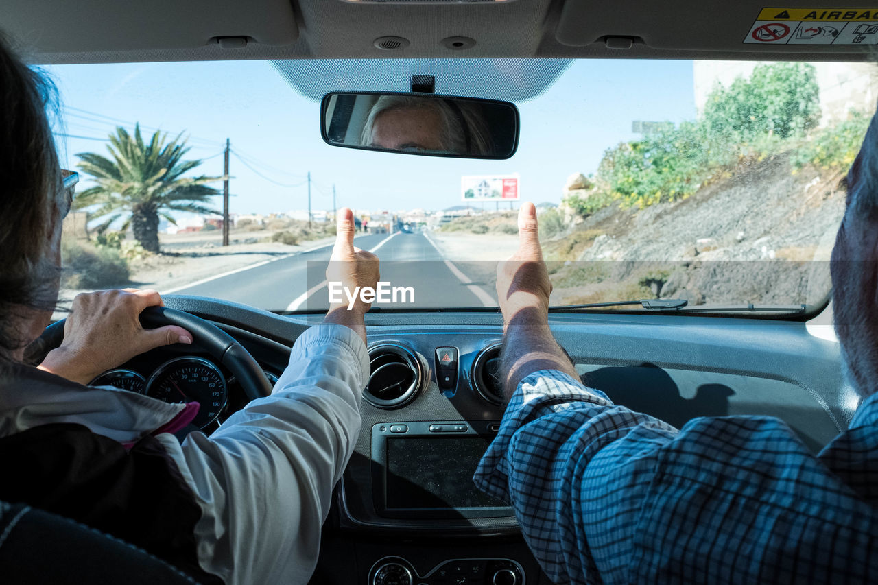 Midsection of couple showing thumbs up while sitting in car