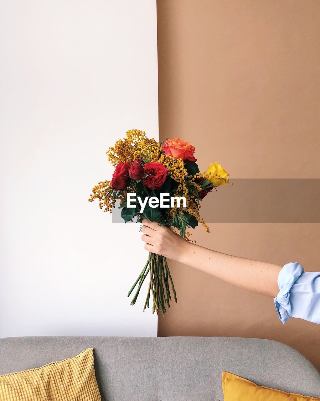 Cropped hand of hand holding bouquet against wall