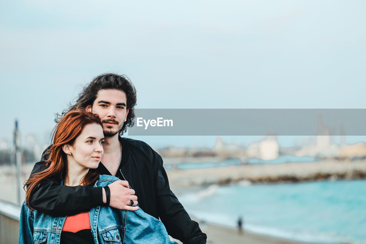 Portrait of man with girlfriend at beach against sky