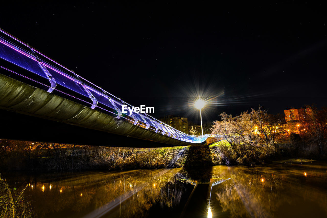 LIGHT TRAILS OVER RIVER AGAINST SKY AT NIGHT