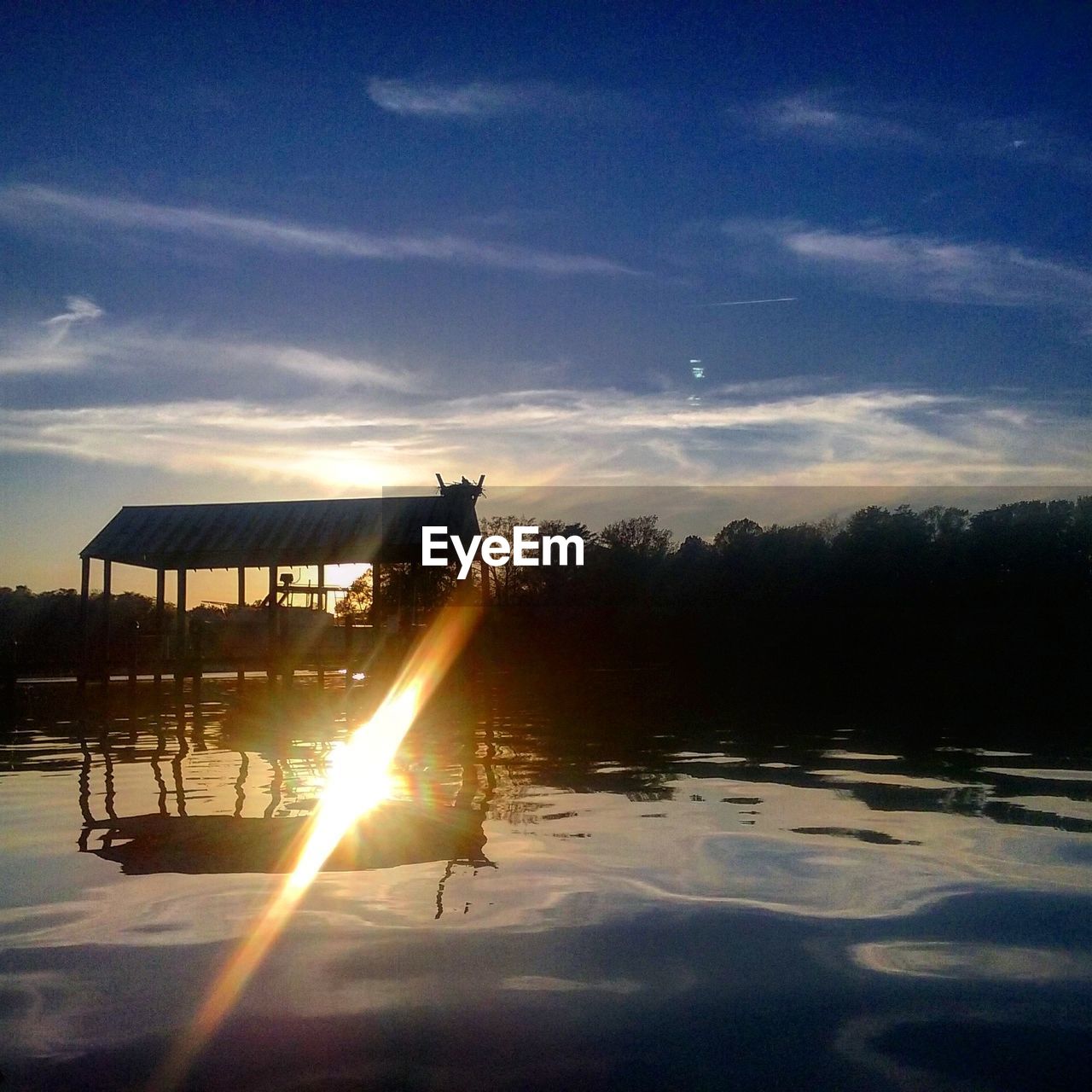 Gazebo in lake with reflection of sun against sky