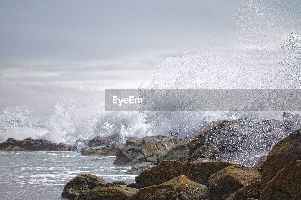 Waves splashing on rocks in sea against sky