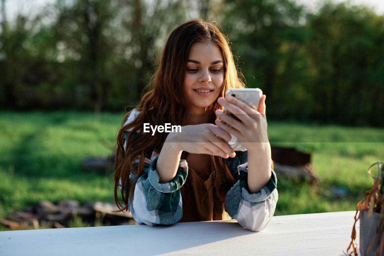 young woman using mobile phone while sitting outdoors