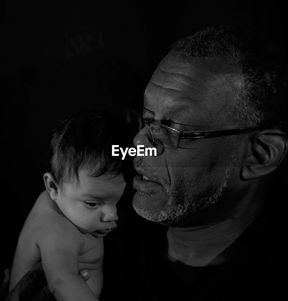 Close-up of father carrying baby boy against black background