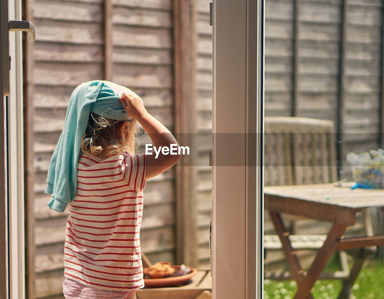 Rear view of girl standing against window at home