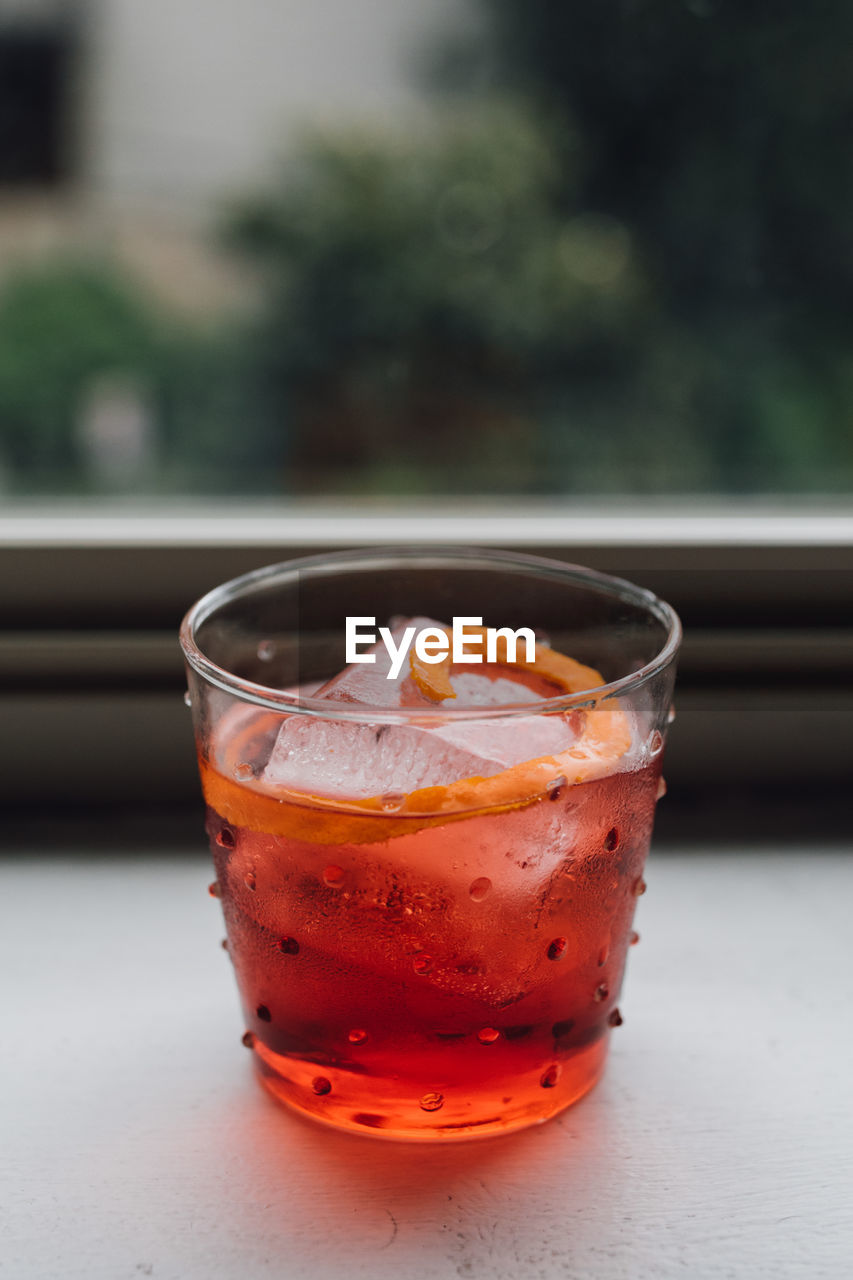 Electric red orange negroni cocktail in polka dot glass on window sill with lush green background